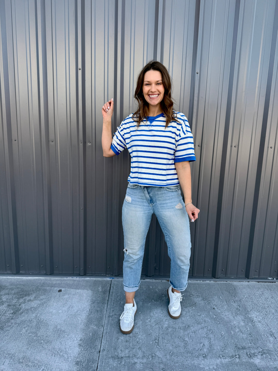 Woman wearing a striped shirt and jeans standing in front of a gray wall.