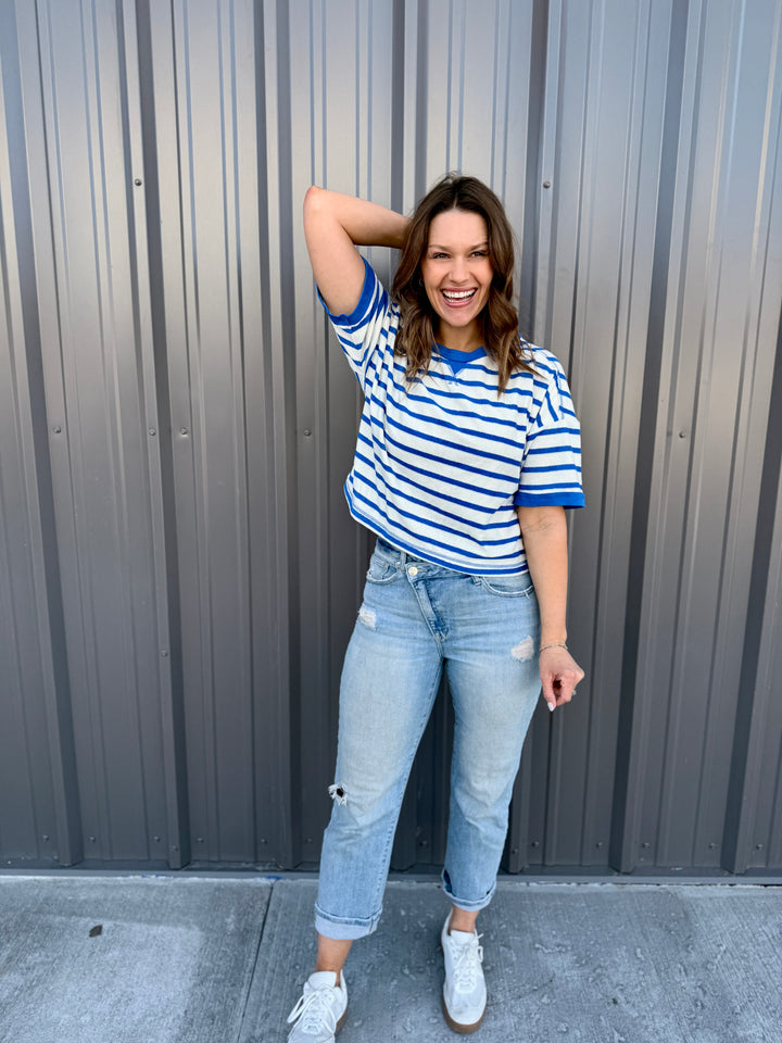 Woman wearing a blue and white striped shirt and jeans standing against a gray metal wall.