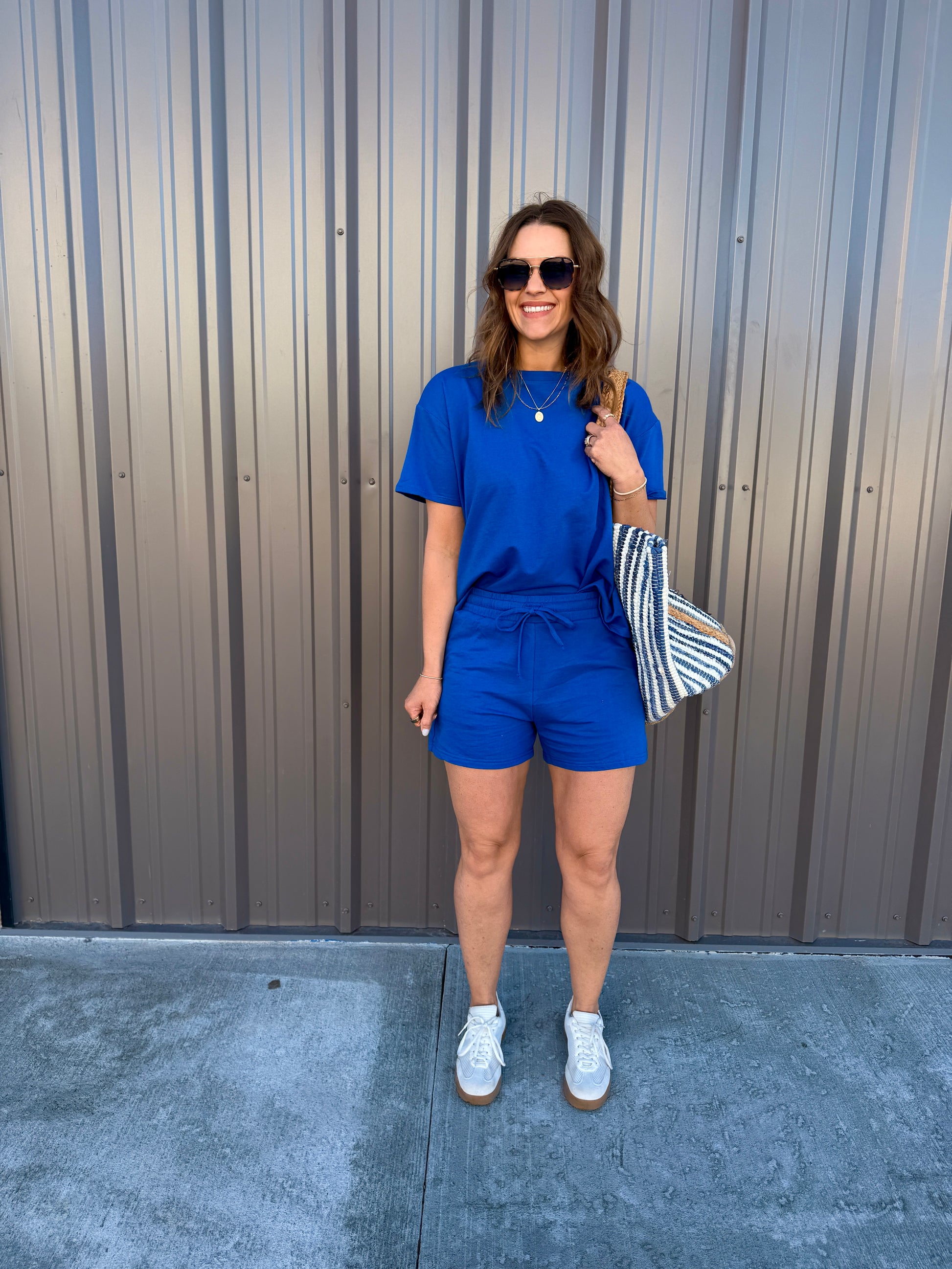 Woman in a blue outfit standing against a metallic wall.